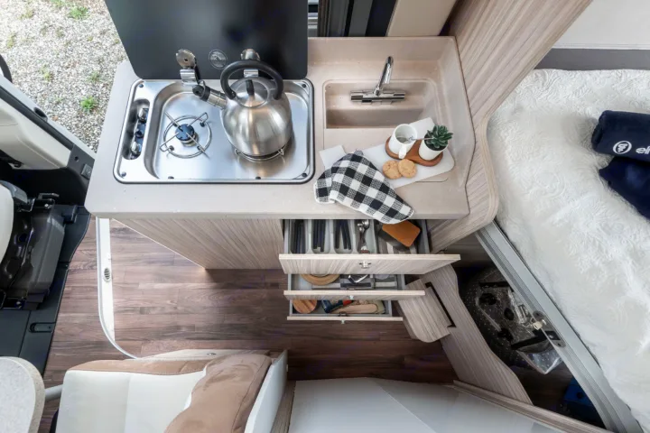 Experience comfort in this RV rental! Overhead view of its compact kitchen with stove, sink, organized drawers, and cozy bed.. ELNAGH DUO XL 2025