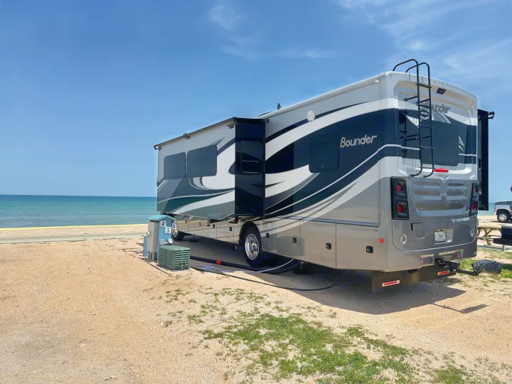 Enjoy a beachfront RV rental experience! A large motorhome is parked at a scenic oceanfront campsite with hookups.. Fleetwood Bounder 33C 2021