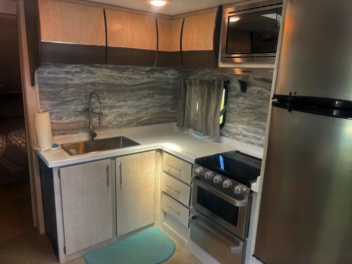 Bright, modern RV rental kitchen showcasing a sink, stainless steel appliances, and elegant marbled backsplash.. Travel Lite Evoke 2020
