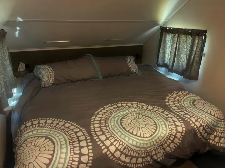 Cozy RV rental bedroom features a large bed with grey patterned bedding and side windows.. Travel Lite Evoke 2020