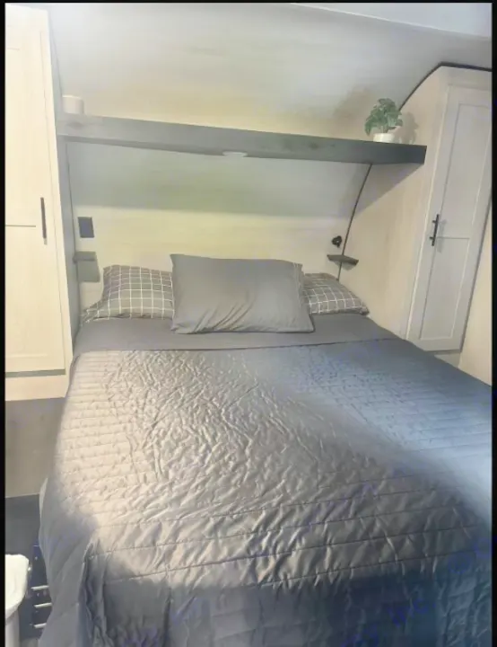 Comfortable RV rental bedroom featuring a large bed with grey bedding, overhead shelf, and side cabinets.. Sportsmen by KZ 250THLE 2022