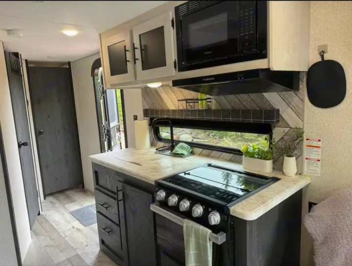 RV rental kitchen interior: Modern galley with dark cabinetry, light countertops, stove, microwave, and sink. Bright and inviting.. Sportsmen by KZ 250THLE 2022