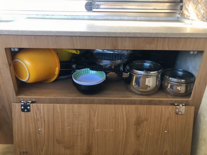 An RV rental's kitchen cabinet filled with essentials: yellow bowls, stacked dishes, and shiny pots & pans for meals on the go.. Fleetwood santa fe 2008