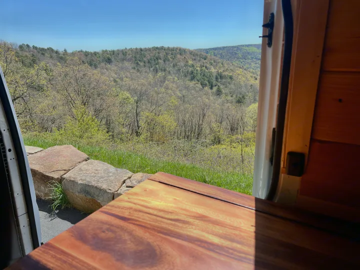 An RV rental provides this stunning spring mountain view. Light green trees fill the valley, framed by a cozy wooden interior.. Dodge Sprinter 3500 2007