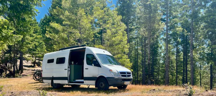 White RV rental camper van in a sunny forest. Bicycles mounted on back for outdoor adventures.. Dodge Sprinter 3500 2007