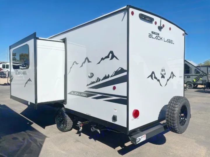 A white Black Label rv rental, an off-road travel trailer, features an open slide-out, rear spare tire, and mountain decals.. Cherokee WOLF PUP BLACK LABEL 17JWBL 2025