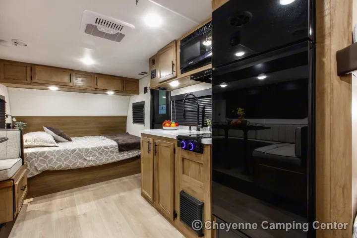 Modern RV rental interior featuring a compact kitchen with sink, microwave, and fridge, plus a cozy bedroom area with bed.. Cherokee WOLF PUP BLACK LABEL 17JWBL 2025