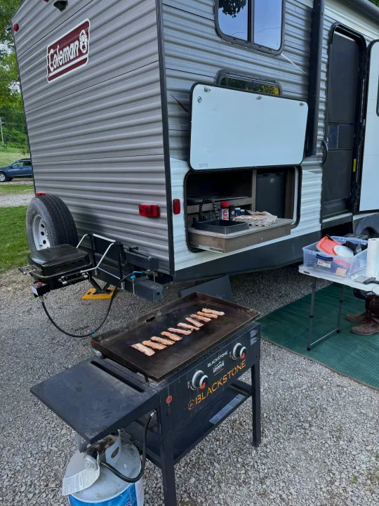 RV rental with an amazing outdoor kitchen featuring a Blackstone griddle cooking bacon, a sink, and a mini-fridge.. Dutchmen Coleman Lantern 2019