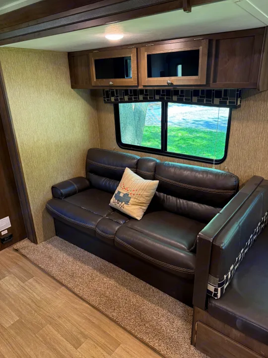 RV rental's inviting interior: A dark leather sofa, dinette, and overhead cabinets offer comfort with scenic window views.. Dutchmen Coleman Lantern 2019