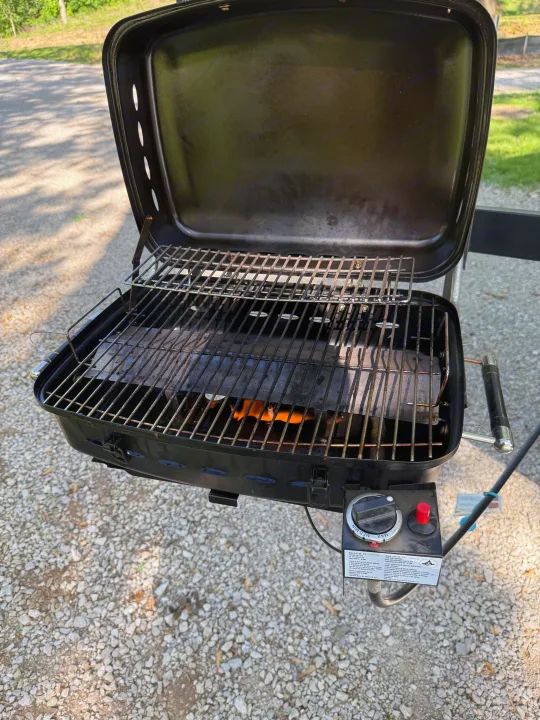 A black portable gas grill, with flames visible, on gravel, perfect for outdoor cooking during your RV rental.. Dutchmen Coleman Lantern 2019