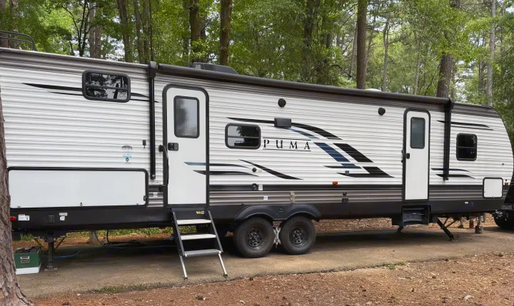 Spacious PUMA travel trailer parked at a wooded campsite, ideal for an RV rental. Ready for your next outdoor adventure!. Forest River Palomino Puma 2021