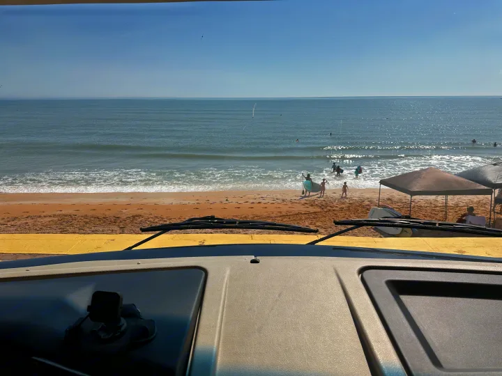 Waterfront RV rental view: sandy beach, ocean waves, and people enjoying the sunny shore from the dashboard perspective.. Fleetwood Bounder 33C 2021