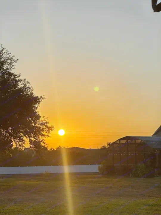 Vibrant sunset, sun flare, and an optical green orb over silhouetted trees and property. Ideal for your next RV rental escape!. Aspen Trail Aspen Trail Trailer 2022