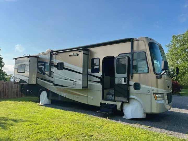 Spacious beige RV rental with extended slide-outs, open door, and tire covers, parked on asphalt.. Allegro Tiffin Allegro Open Road 2012