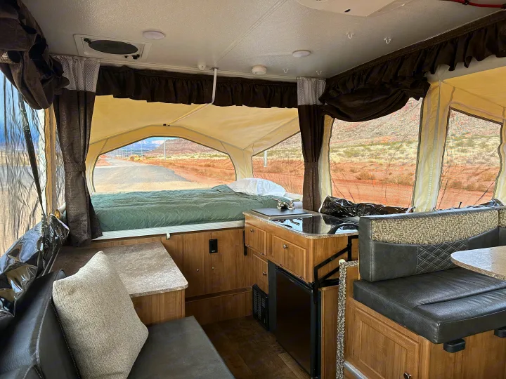 Interior of an RV rental pop-up camper, featuring a bed, kitchenette, dinette, and scenic outdoor views.. Forest River Rockwood Premier 2017