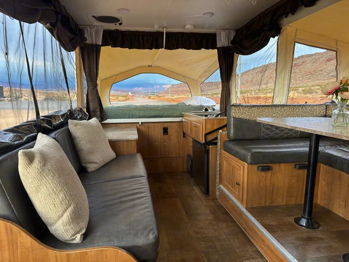 Inside a comfortable rv rental: sofa, dinette, kitchen, and bed. Large screened windows reveal a stunning desert road view.. Forest River Rockwood Premier 2017