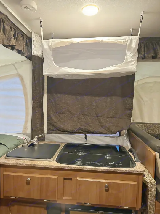 Inside an RV rental: Compact kitchenette with a two-burner stove, sink, and pop-up canvas walls. Ideal for camping.. Forest River Rockwood Premier 2017