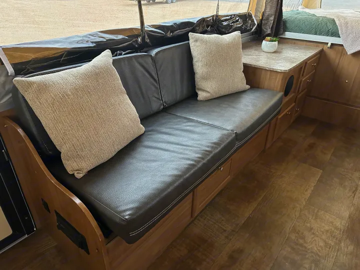 Cozy RV rental interior with a black sofa, two pillows, wood-look floor, compact counter, and visible bed area.. Forest River Rockwood Premier 2017