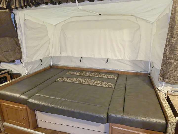 Experience comfort in this RV rental! View of the interior's pop-up bed, featuring dark leather-like cushions.. Forest River Rockwood Premier 2017