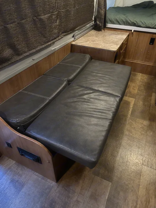 RV rental interior: a versatile dark faux leather couch/bed, wood cabinets, and cozy sleeping area in a pop-up camper.. Forest River Rockwood Premier 2017