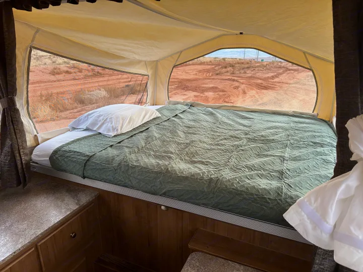 Inside a pop-up RV rental, featuring a comfortable bed overlooking a dry, open landscape.. Forest River Rockwood Premier 2017