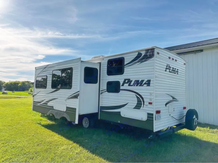 Explore the outdoors with this PUMA travel trailer RV rental, featuring a slide-out, parked on green grass.. Forest River Palomino Puma 2013