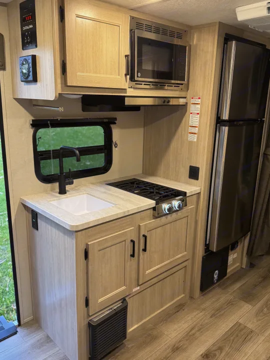 This RV rental showcases a compact kitchen with a sink, two-burner stove, microwave, refrigerator, and light wood cabinetry.. Forest River 184BHS 2025
