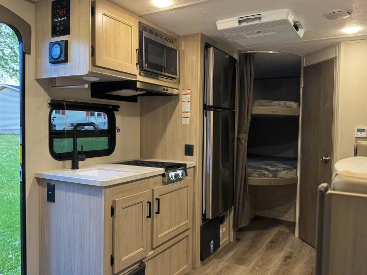Modern RV rental interior with a full kitchen, sleek refrigerator, and cozy bunk beds, ideal for travel.. Forest River 184BHS 2025