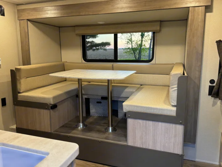 Modern RV rental dinette with light upholstered booth seating, a table, and a window view, offering comfort.. Forest River 184BHS 2025