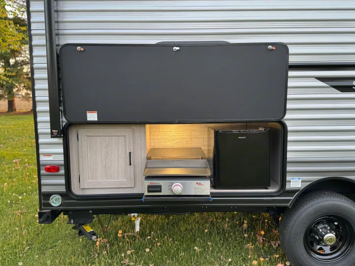 An RV rental's accessible outdoor kitchen compartment, revealing a Hotpoint mini-fridge, Suburban griddle, and a cabinet.. Forest River 184BHS 2025