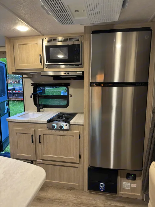 Modern RV rental kitchen with stainless steel GE appliances (fridge, microwave, cooktop), sink, and light wood cabinetry.. Forest River 184BHS 2025
