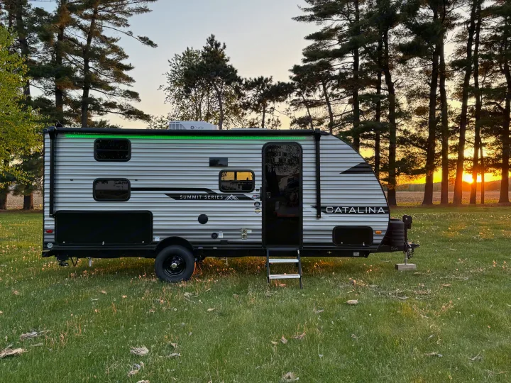 RV rental: Catalina Summit Series travel trailer parked in a grassy field at sunset, among pine trees.. Forest River 184BHS 2025