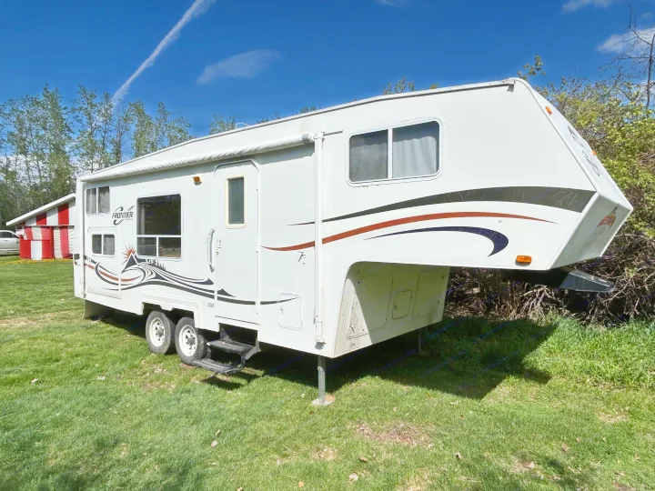 This white Frontier fifth-wheel RV rental is parked on grass under a blue sky, ready for your next outdoor adventure.. Frontier FW255 2012