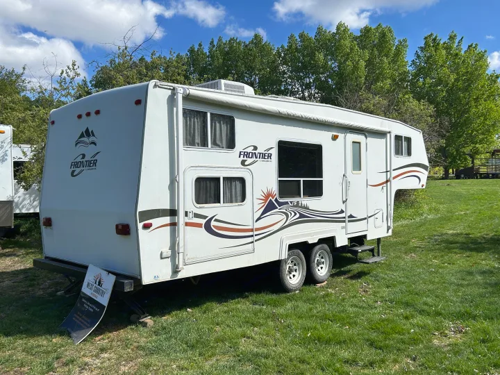 A white Frontier RV rental for outdoor adventures, parked in a grassy field with trees and a bright blue sky.. Frontier FW255 2012
