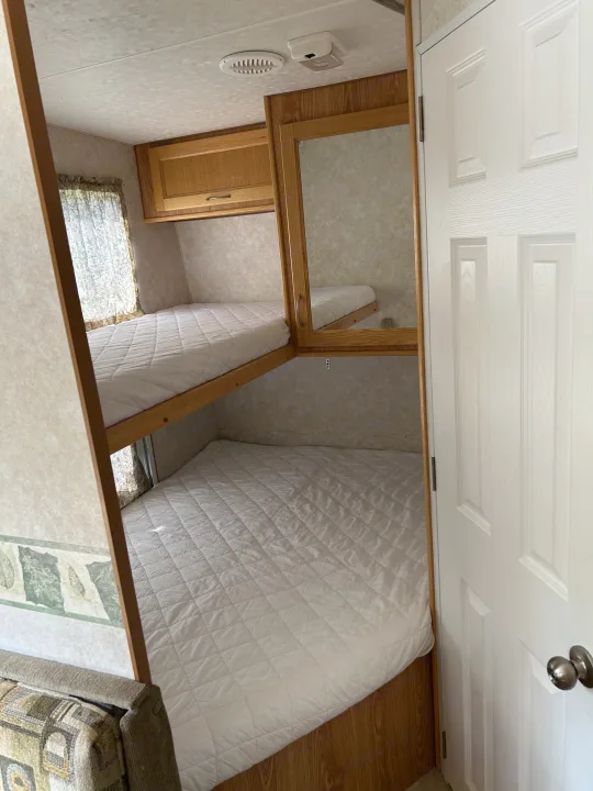 Inside an RV rental: clean bunk beds with white mattresses, a mirrored cabinet, a window, and a white door.. Frontier FW255 2012