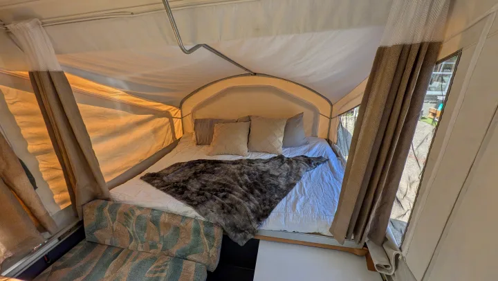 Relax in this RV rental's cozy pop-up camper interior, featuring a plush bed, soft pillows, and charming curtains.. Coachmen Clipper 2008