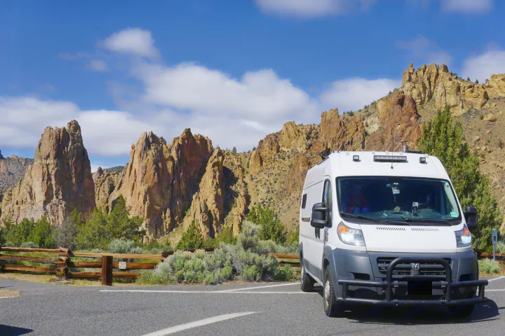 Scenic view: a white camper van, perfect for RV rental, parked amidst towering rock formations under a blue sky.. Ram promaster 2500 2017