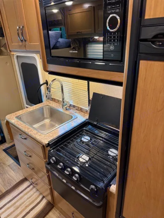 Well-equipped RV rental kitchen featuring a sink, 3-burner gas stove, microwave, fridge, and ample storage cabinets.. Thor Freedom Elite 2017