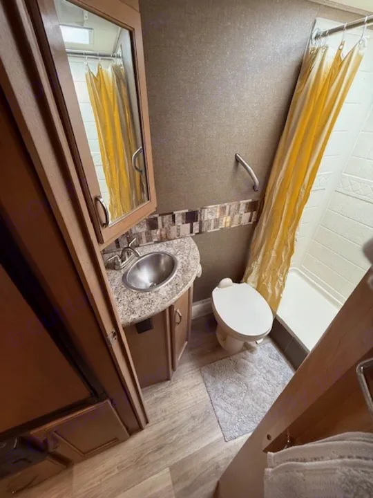 RV rental bathroom: compact space with sink, toilet, and shower featuring a bright yellow curtain.. Thor Freedom Elite 2017