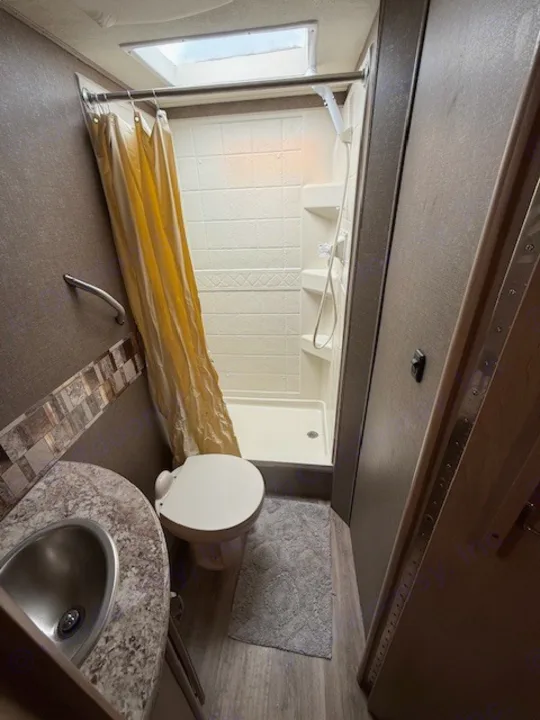 RV rental bathroom with a compact sink, toilet, and shower stall, featuring a skylight for natural light.. Thor Freedom Elite 2017