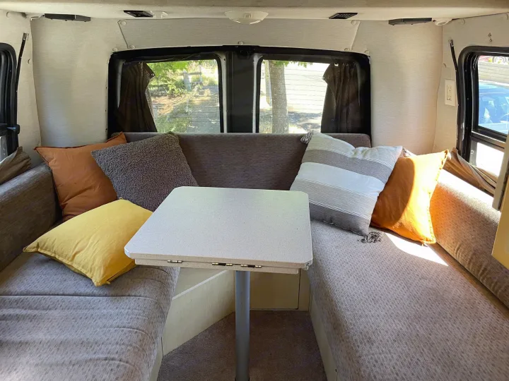 Cozy RV rental interior featuring a U-shaped dinette with cushions & central table, offering outdoor views.. Roadtrek 210 - Popular 2005