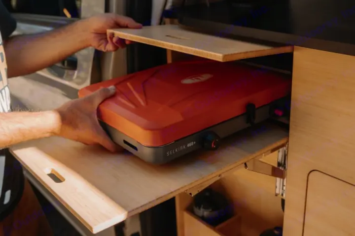 Person retrieves a bright orange Selkirk portable stove from slide-out storage in an RV rental. Ready for cooking on the go.. Mercedes-Benz metris 2022