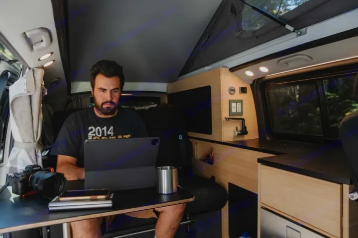 Inside a well-equipped RV rental, a man works on his laptop, embracing the digital nomad lifestyle.. Mercedes-Benz metris 2022