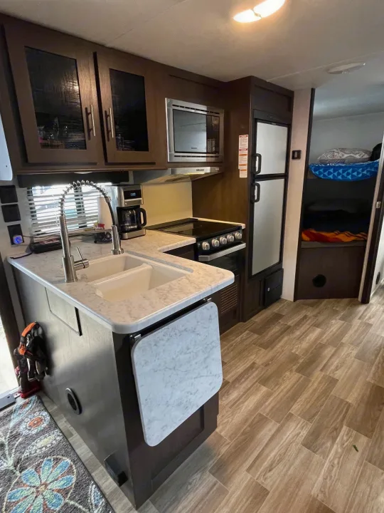 RV rental kitchen: white marble-look counters, sink, stove, microwave, and fridge. Compact for travel.. Forest River Salem Cruise Lite 2020