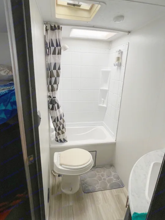 A compact RV rental bathroom showing a shower/tub combo, toilet, sink, and geometric shower curtain.. Forest River Salem Cruise Lite 2020