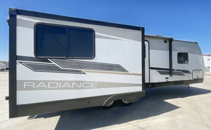 A white, gray, and black Radiance travel trailer with its slide-out extended, ideal for an rv rental adventure.. Cruiser RV Radiance 2022