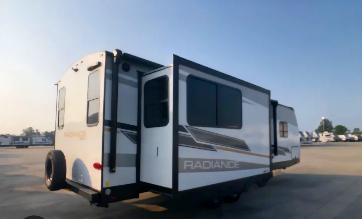 A white and gray travel trailer RV rental with extended slide-outs parked in a lot, showcasing its spacious design.. Cruiser RV Radiance 2022
