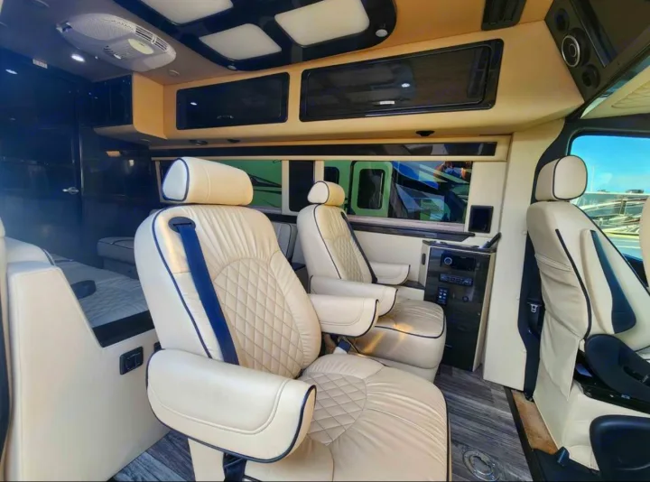 Plush cream leather captain's chairs inside a high-end RV rental van, with ceiling lights & wood-look floor.. Ultimate Toys Ultimate RV 2021