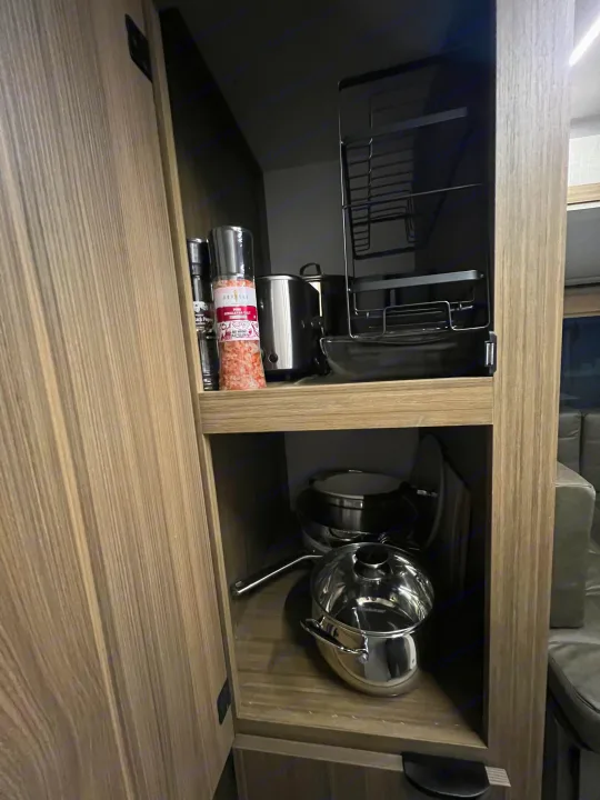 Compact RV rental kitchen storage featuring spices, small appliance, and shiny pots & pans neatly stowed away in the cabinet.. Forest River 28VBXLX 2025