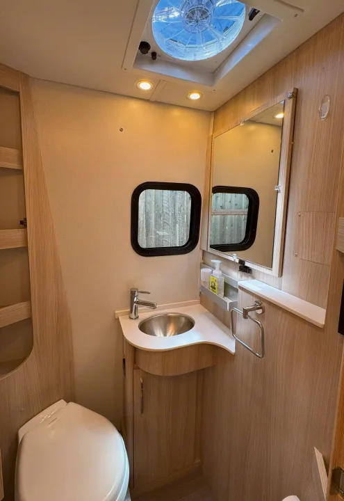 Compact RV rental bathroom features a toilet, sink with mirror, and an overhead vent fan for convenient travel.. Leisure Travel Vans Unity 2022